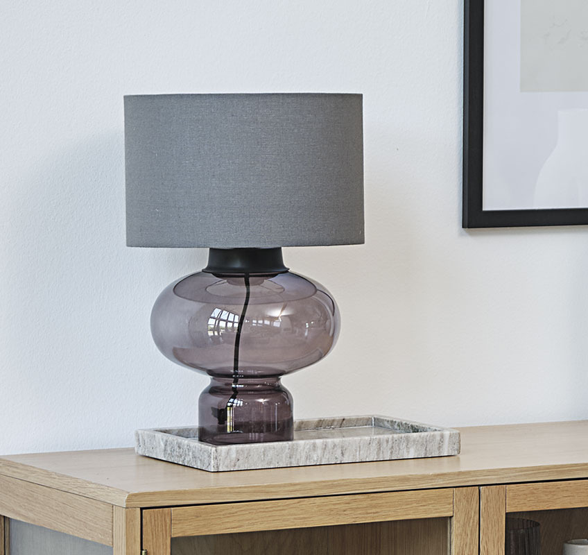 Bordslampa med glasfot och grå lampskärm på marmorbricka