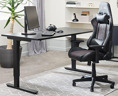 Höj- och sänkbart skrivbord med en svart gamingstol i ett hemmakontor 