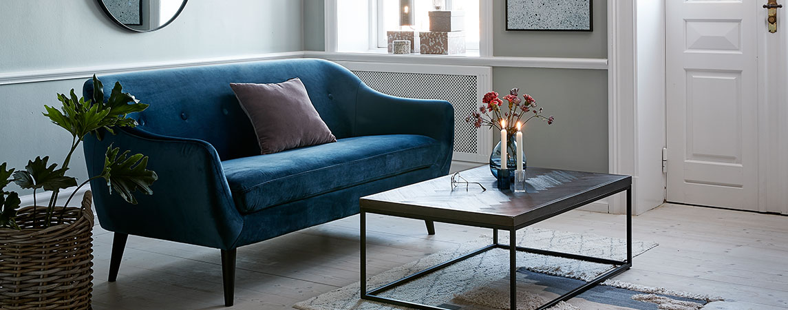Vardagsrum med en blå sammetssoffa och ett soffbord med tända ljus