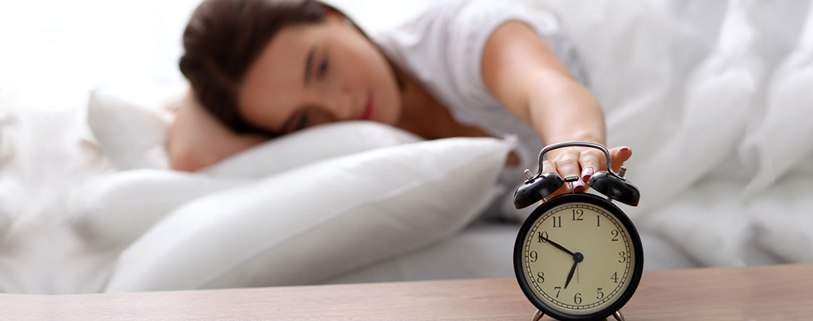 Kvinna som sover i sängen och sträcker ut armen för att stänga av väckarklockan