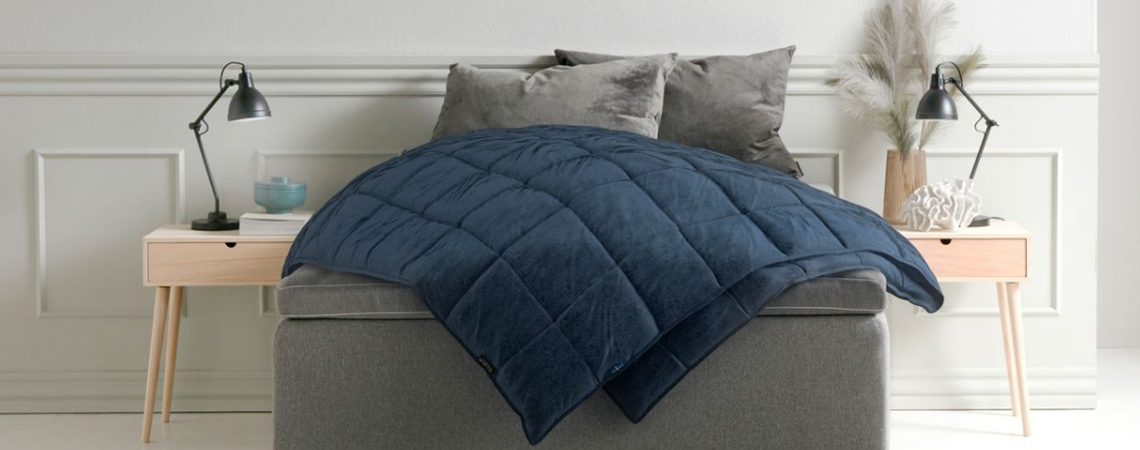 En mörkblå tyngdfilt som ligger på en säng 
