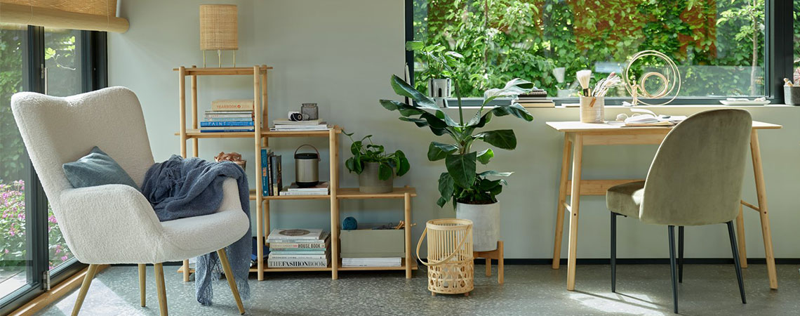 Grå fåtölj vid ett fönster och en rumsdelare i bambu i bakgrunden. Bambu lykta på golvet bredvid ett bambu skrivbord och en olivgrön matstol