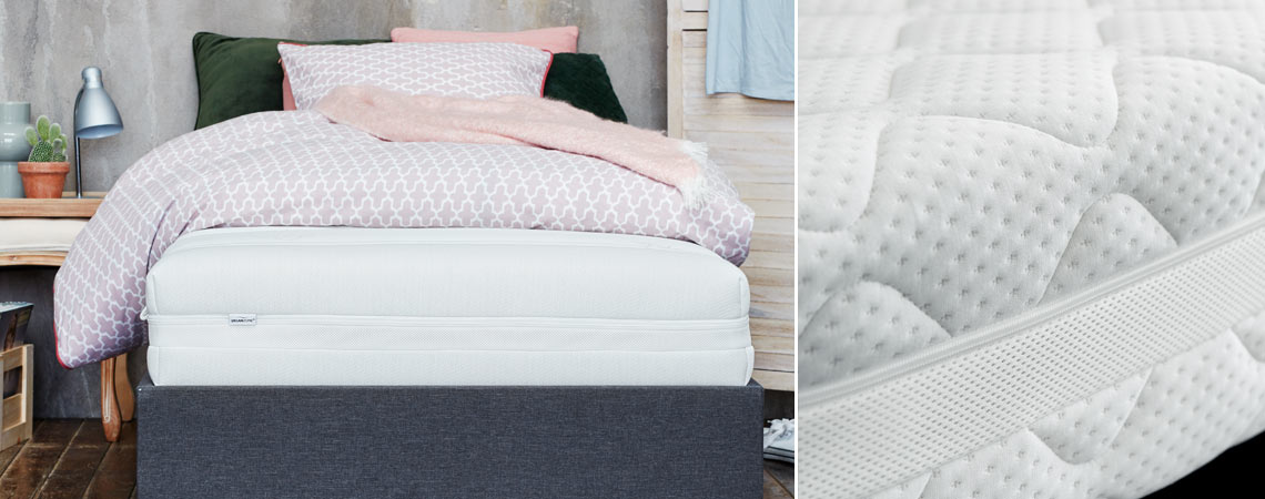grå sängram med vit skummadrass med täcke och kuddar i olika färger 