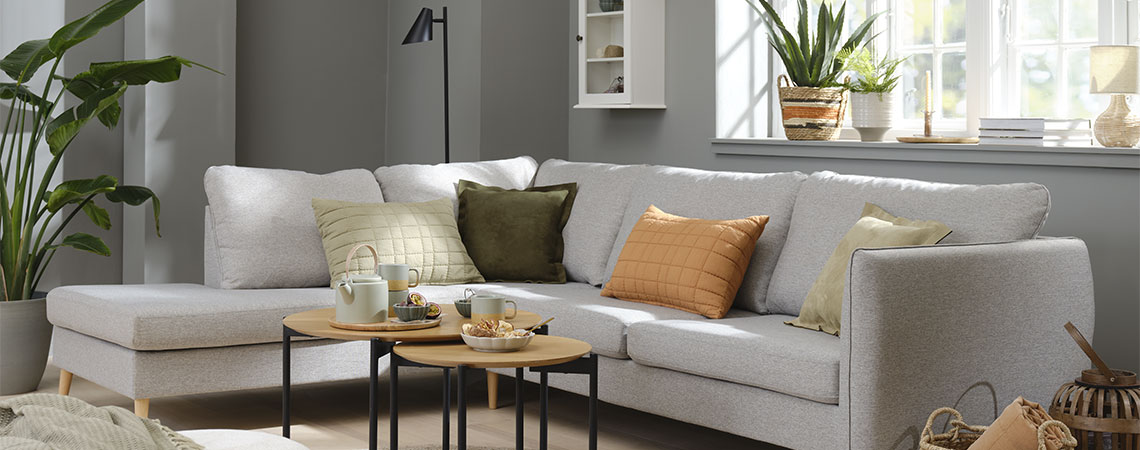 Vardagsrumsmiljö med grå soffa och orange, gröna och beige kuddar