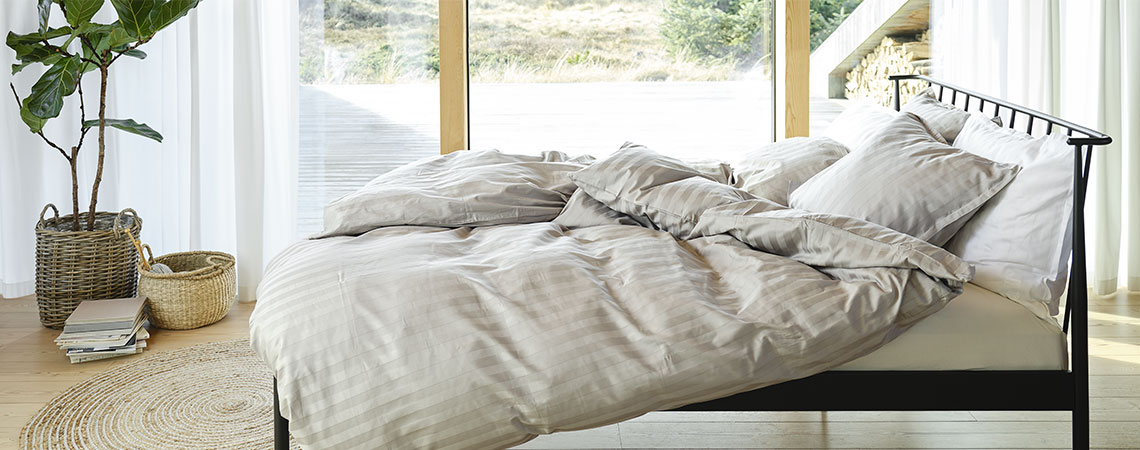 Sovrum med svart metallsäng, täcken och kuddar, klädd i randigt sängkläder i ljusgrått och vitt