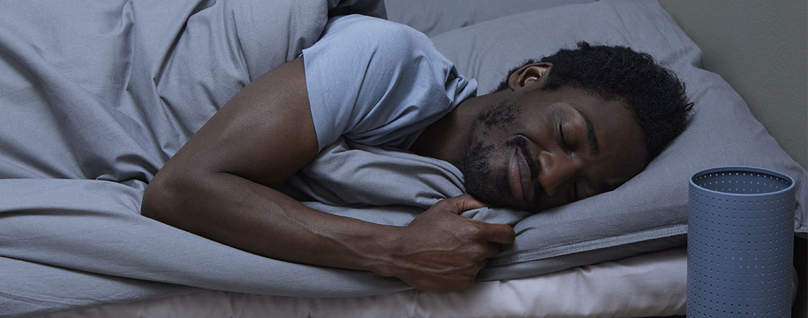 Man sover i sängen med grå kudde och ett grått täcke