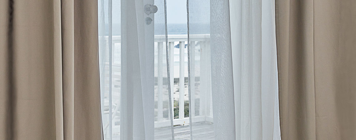 Utsikt till en balkong genom en öppen dörr med fladdrande gardiner