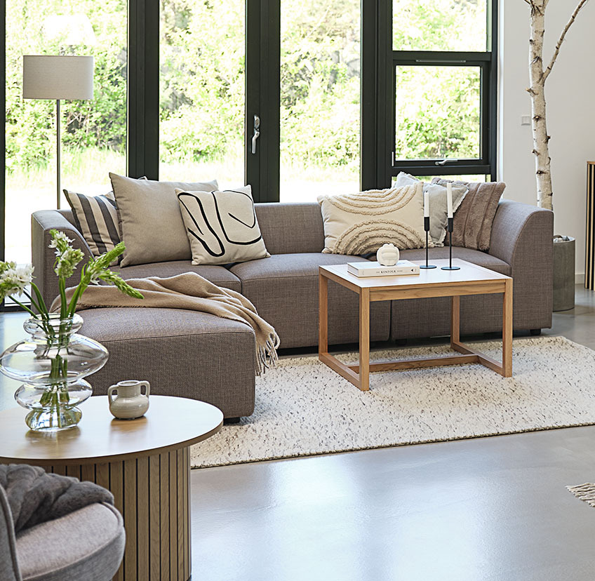 Minimalistiskt soffbord i ek i ljust vardagsrum med stor soffa och dekorativa kuddar