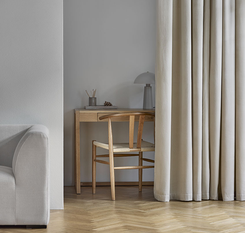 Beige gardiner som skiljer ett hemmakontor med skrivbord och stol från ett vardagsrum