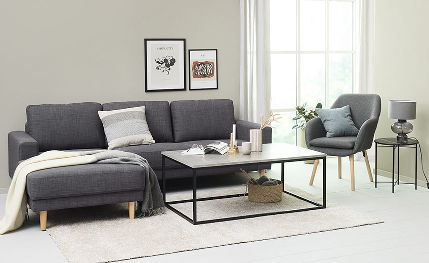 BIRK matta i grå färg Vardagsrum med en ljusgrå matta, en fåtölj och en soffa med en kudde och pläd