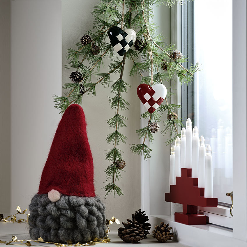 MUGGLESTEN jultomten har ett stort, lockigt skägg Skandinavisk jultomte med grått skägg på en dekorerad fönsterbräda