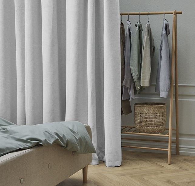 Beige gardin framför en klädstång skiljer en sovplats från en garderobsdel