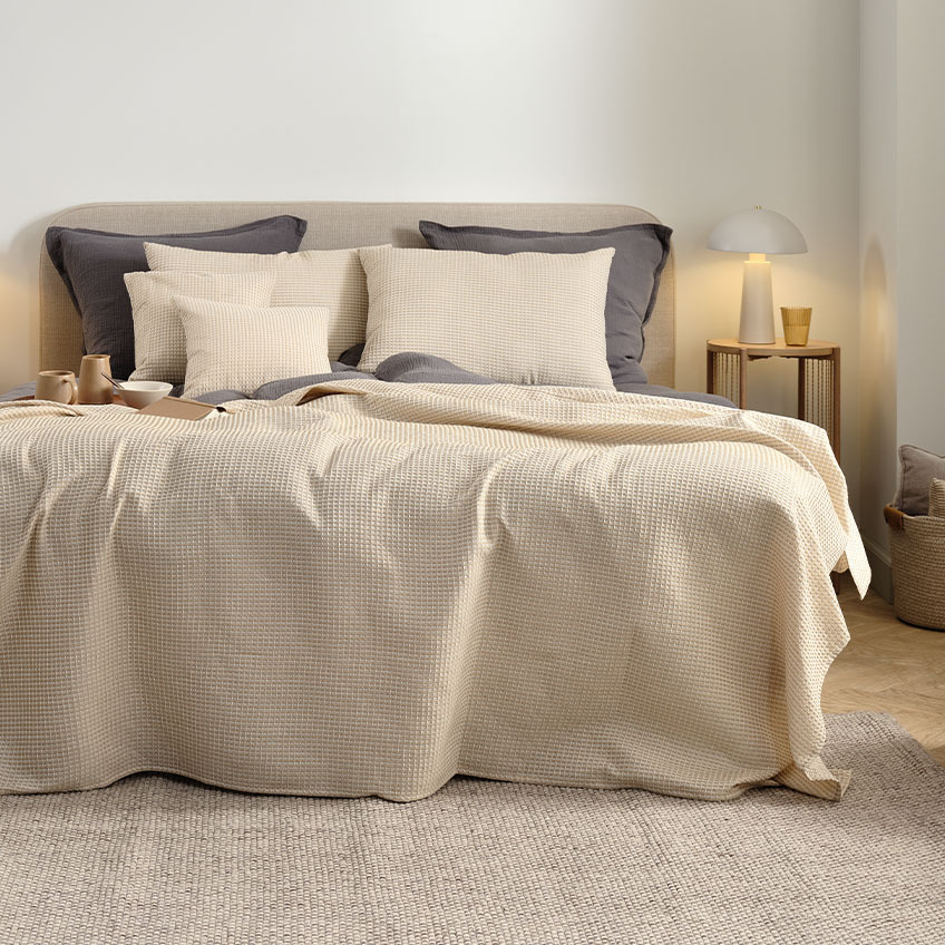Sängöverkast, ryggkuddar och dynor i varm beige färg på dubbelsäng i sovrummet