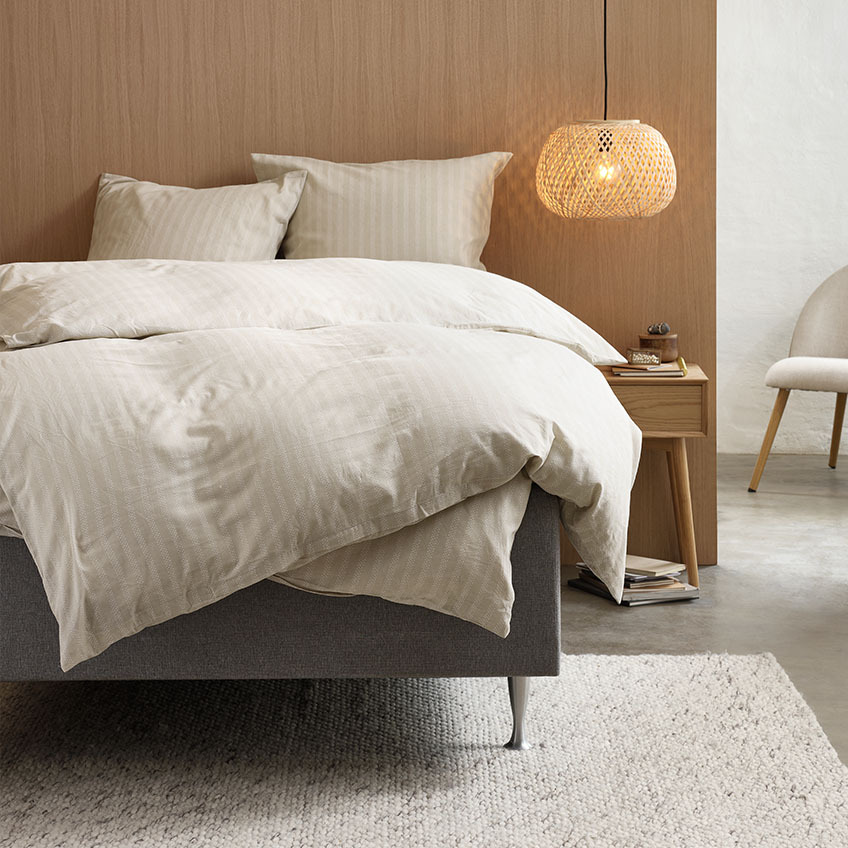 Påslakanset av bomullsflanell i varm beige färg med randig design på sängen i sovrummet