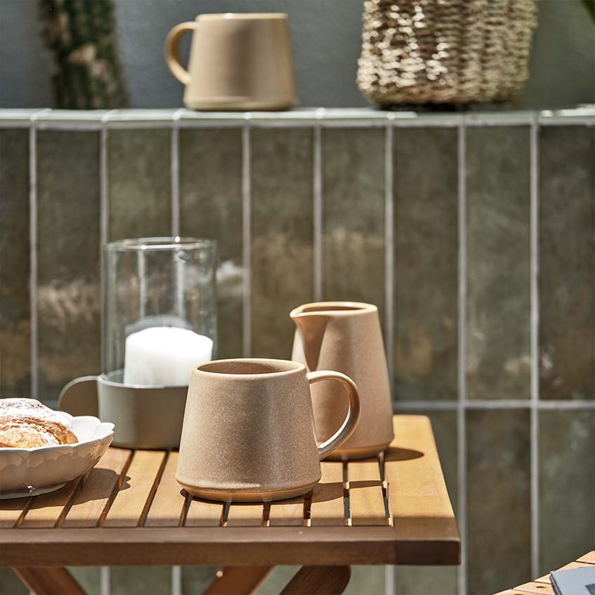 Kaffemugg och mjölkkanna på litet trädgårdsbord av trä i full sol