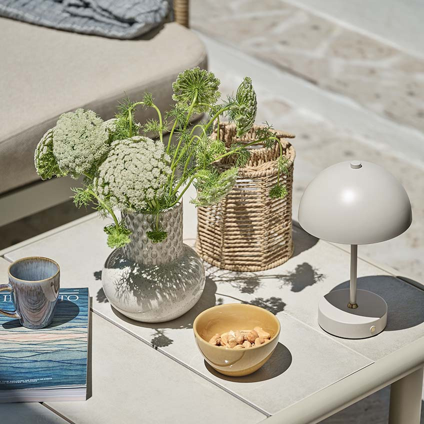 Litet trädgårdsbord med olika dekorer, inklusive liten batterilampa, vas och lykta