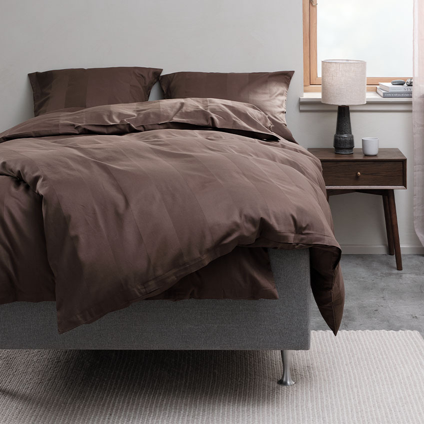 Chokladbrunt påslakanset och sängkläder i bomull på sängen i sovrummet