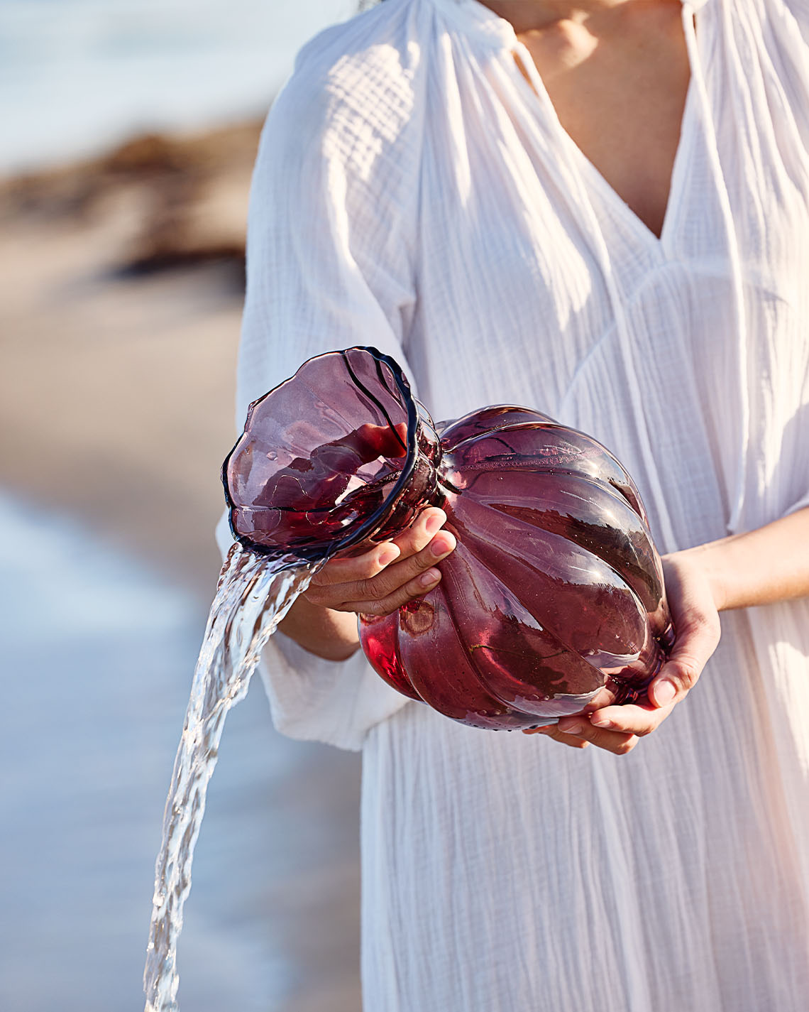 Glasvas i auberginefärg hålls av kvinna på stranden