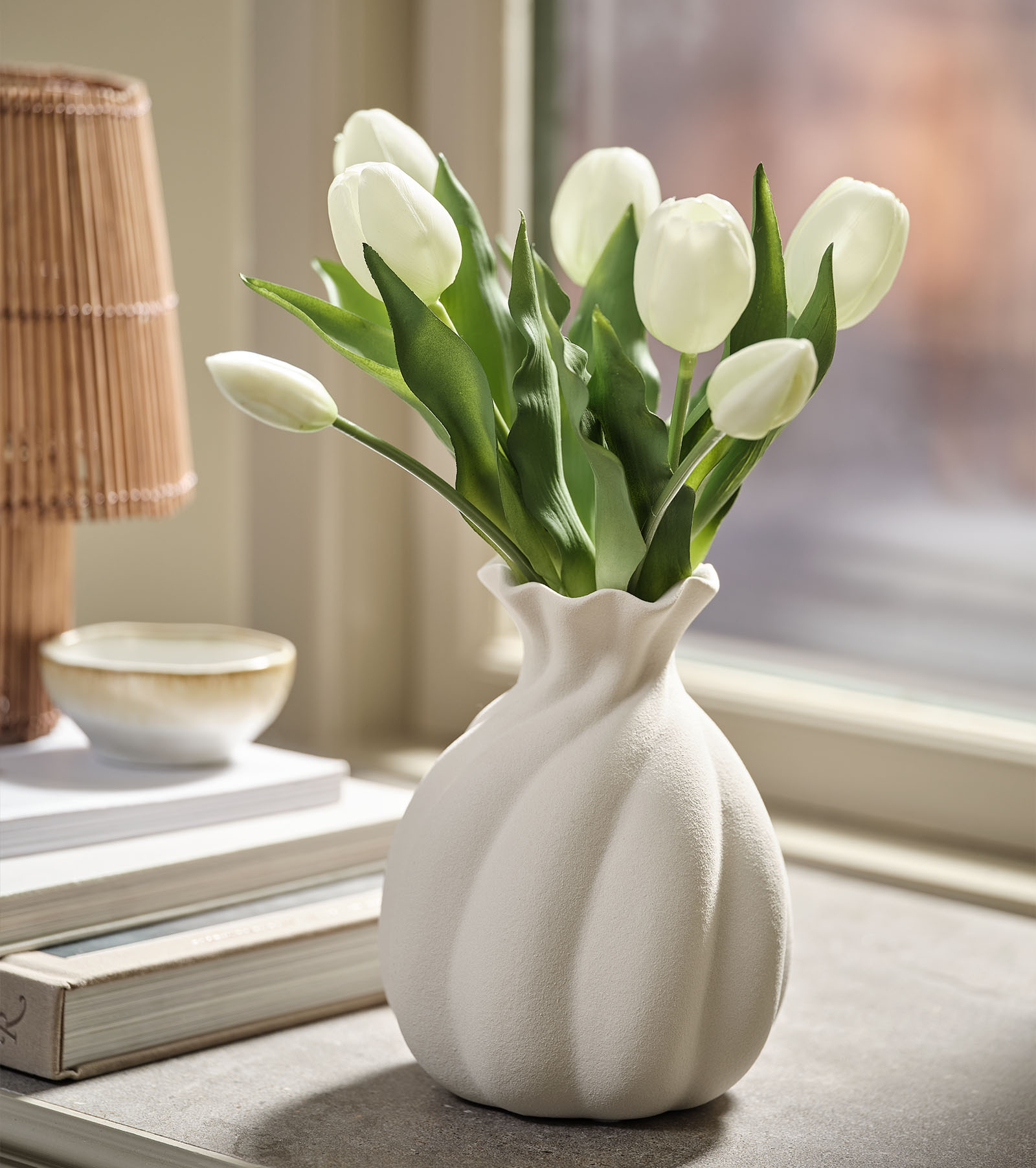 Konstgjord blomsterbukett som imitation av vita tulpaner med gröna blad i en vit vas