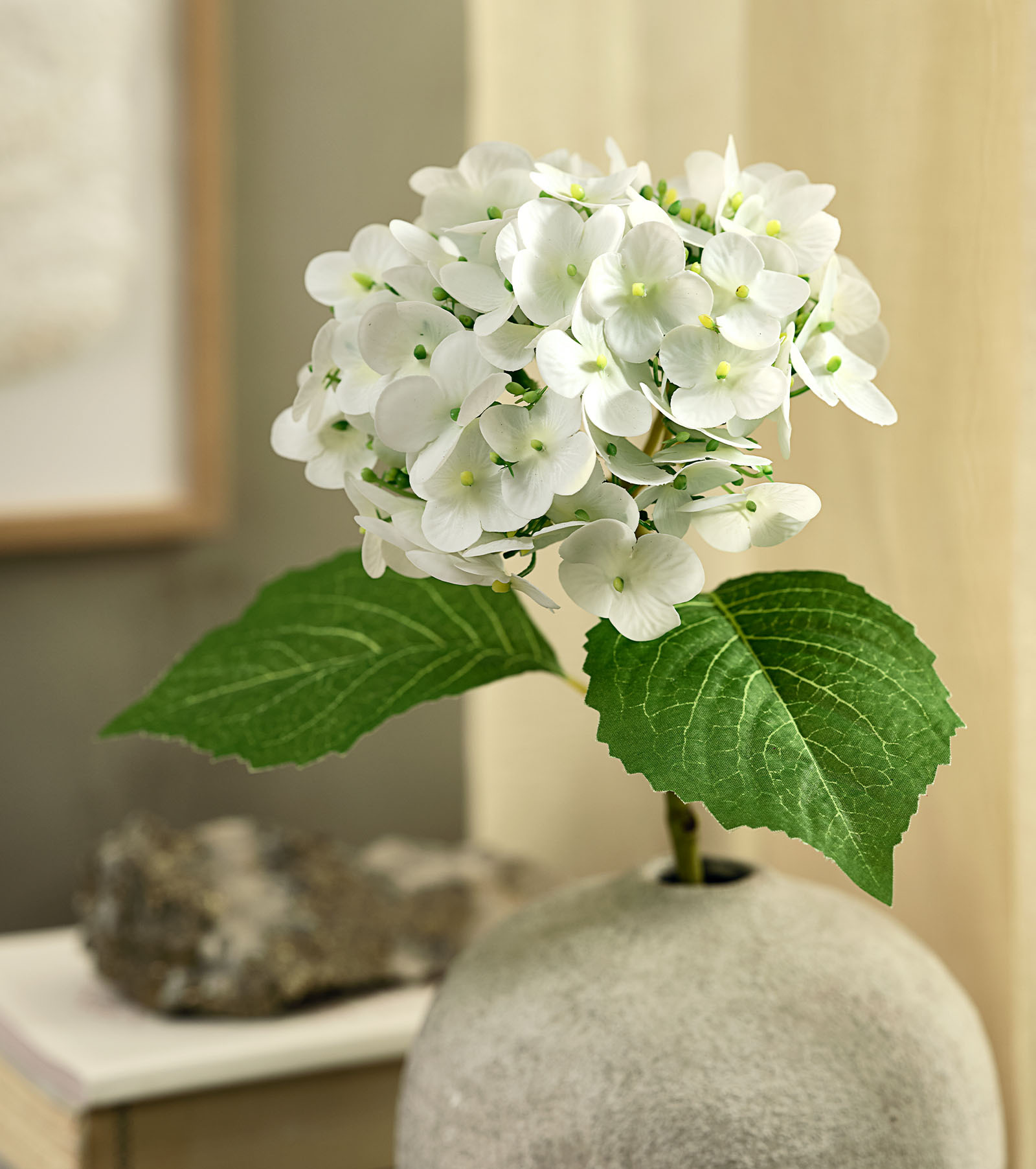 Artificiell blomimitation av en vit hortensia med gröna blad i en rustik vas