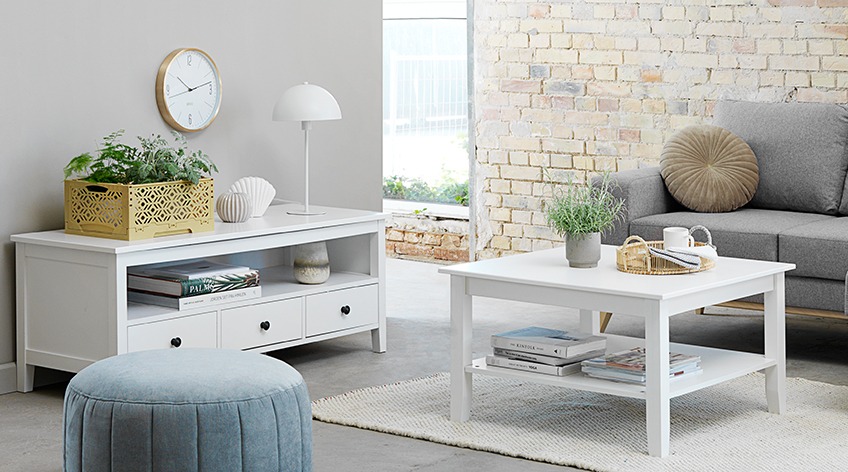 Light living room with white tv stand and coffee table, grey sofa and mint pouffe in the foreground