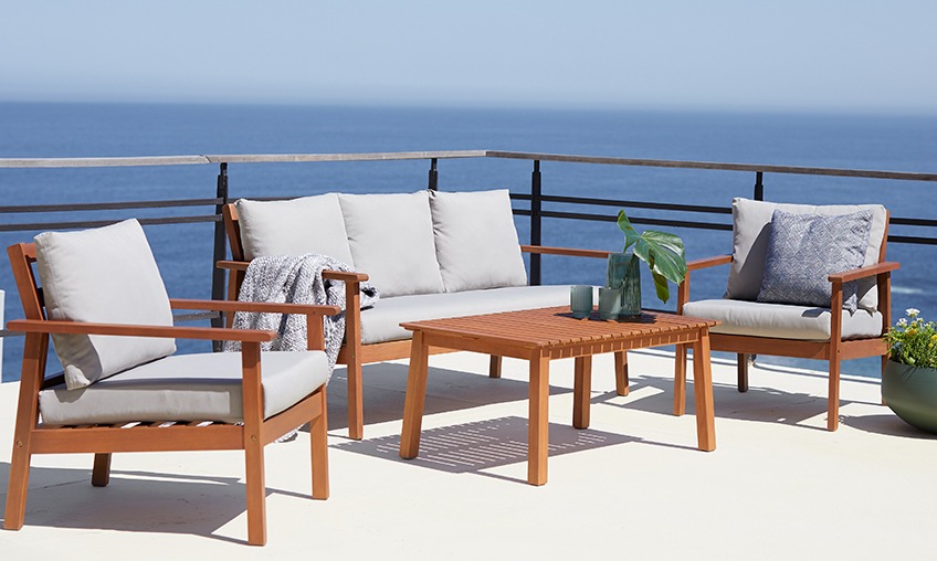 Wooden lounge set with lounge table, lounge sofa and 2 lounge chairs on a patio by the ocean