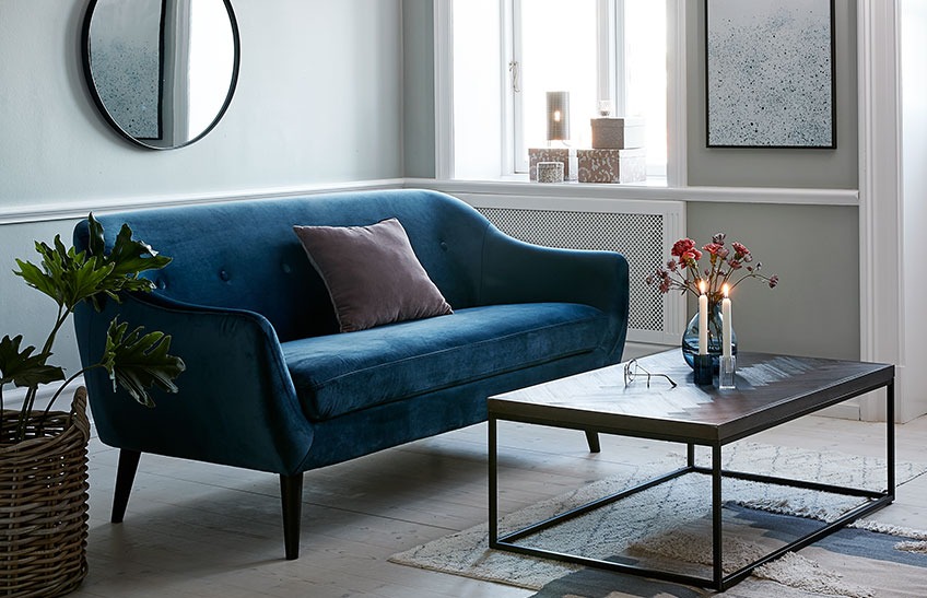A living room with a blue velvet sofa and a coffee table 