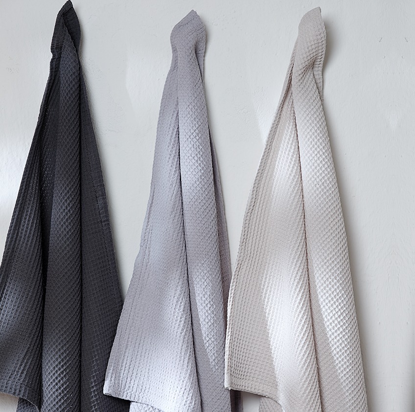 Tea towels in three different colours hanging on a wall 