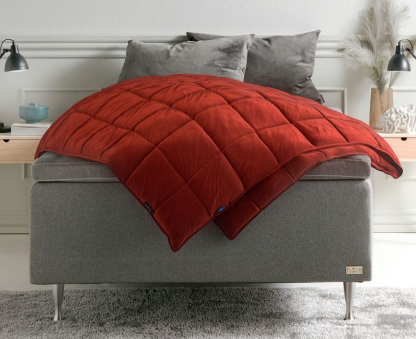 En röd Tyngdpläd på en grå säng i ett sovrum