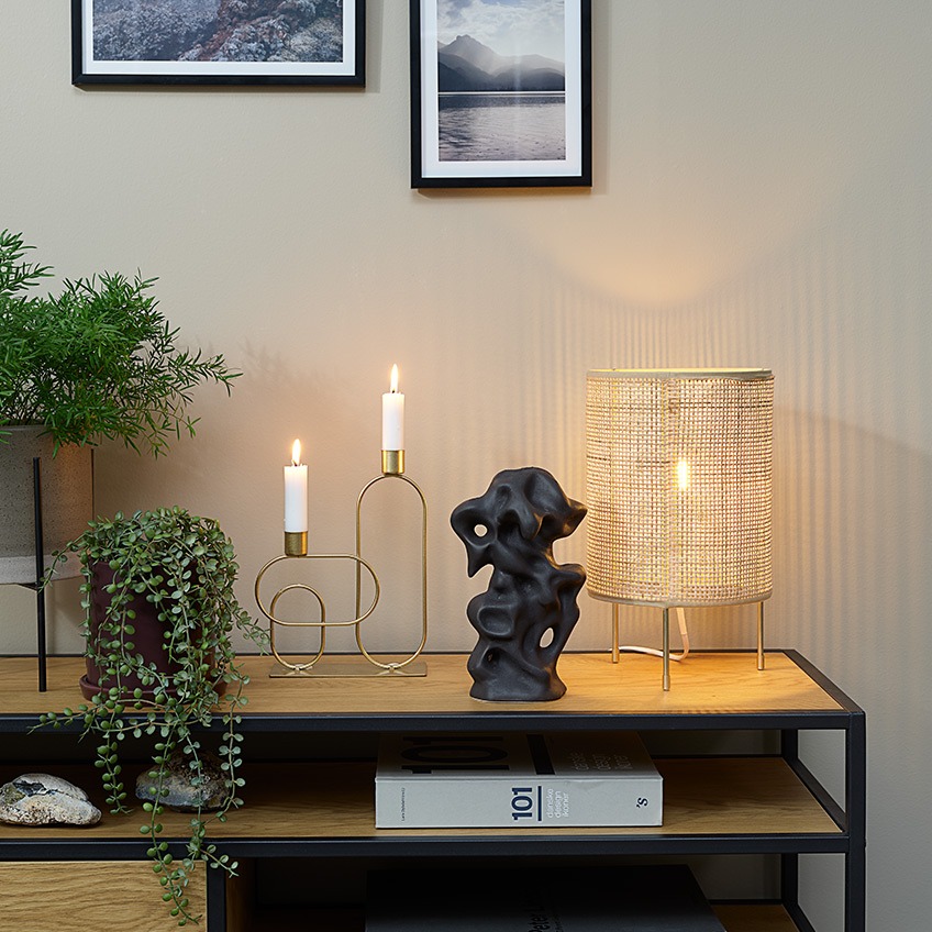Växtkrukor, konstgjorda växter, ljusstake, prydnad och bordslampa ovanpå ett TV-stativ
