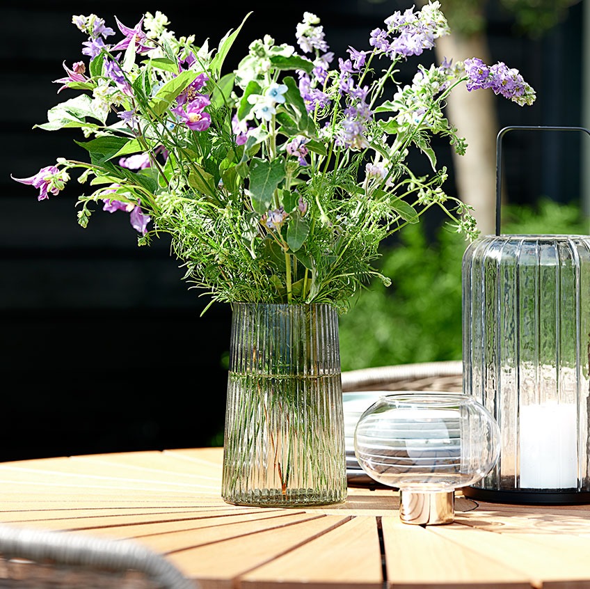 Vas i glas och lyktor på ett trädgårdsbord i teak