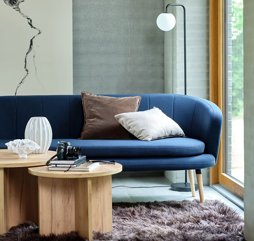 Blå soffa, runda soffbord, brun matta och golvlampa