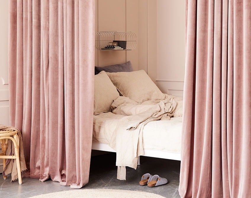 Rosefärgade gardiner som separerar en sovplats från ett stort vardagsrum