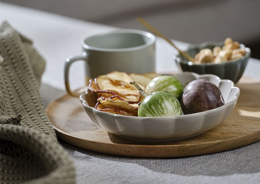 Träbricka med grå skål fylld med frukt placerad på soffan