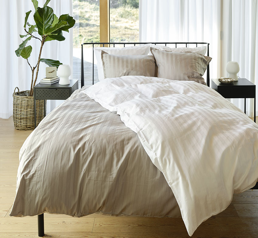 Sovrum med grå- och vitrandiga sängkläder på sängen och två sängbord