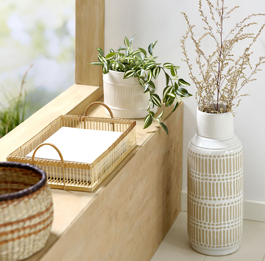 Hög vas vid fönsterbrädan med bambubricka och vit växtkruka med konstgjord växt