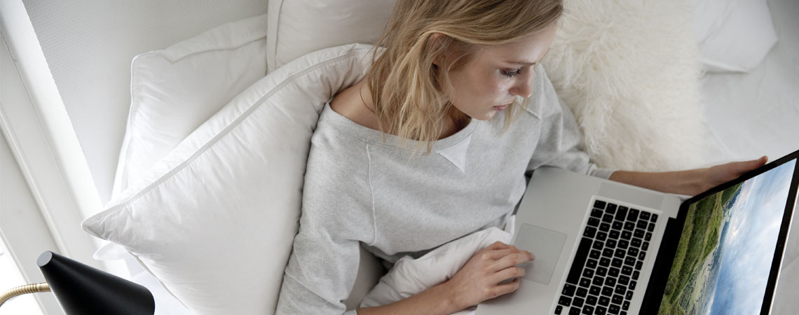 Kvinna sitter med laptop i en säng 