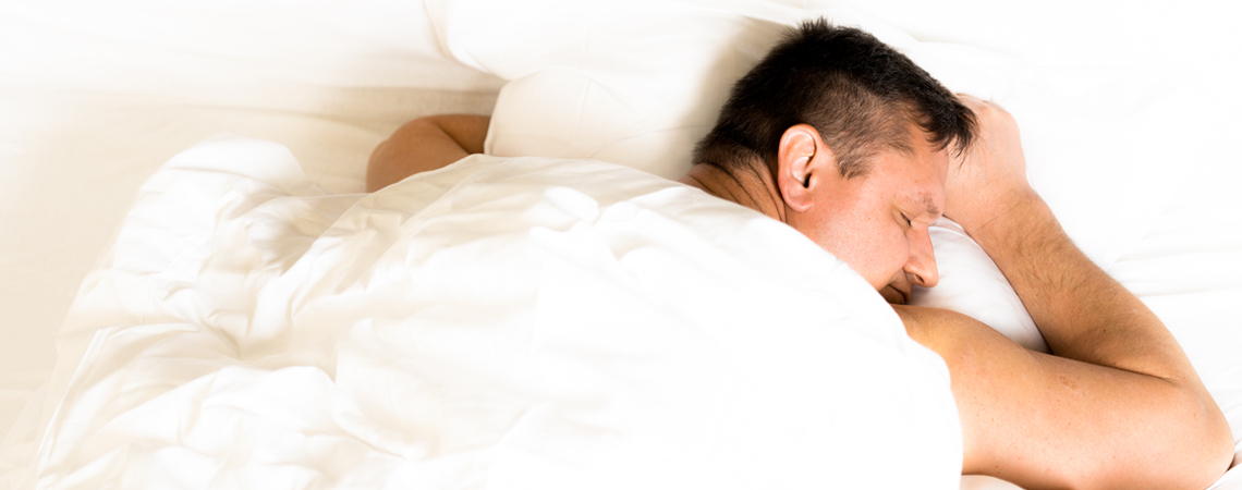 En person sover på magen i sängen 