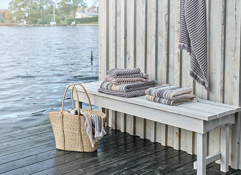 Lyxiga handdukar på en bänk och i en flätad väska vid en sjö