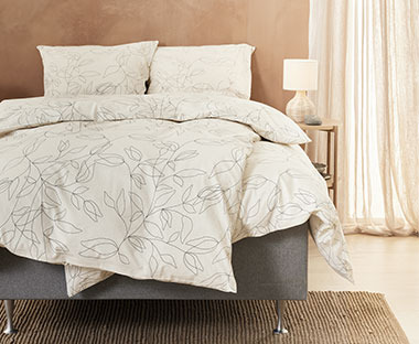 SVEA sängkläder i ljusa färger i ett sovrum med ett sängbord bredvid 