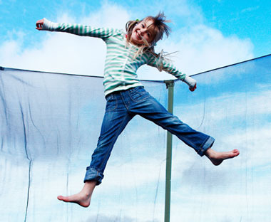 Flicka hoppar i en studsmatta med säkerhetsnät och är glad 